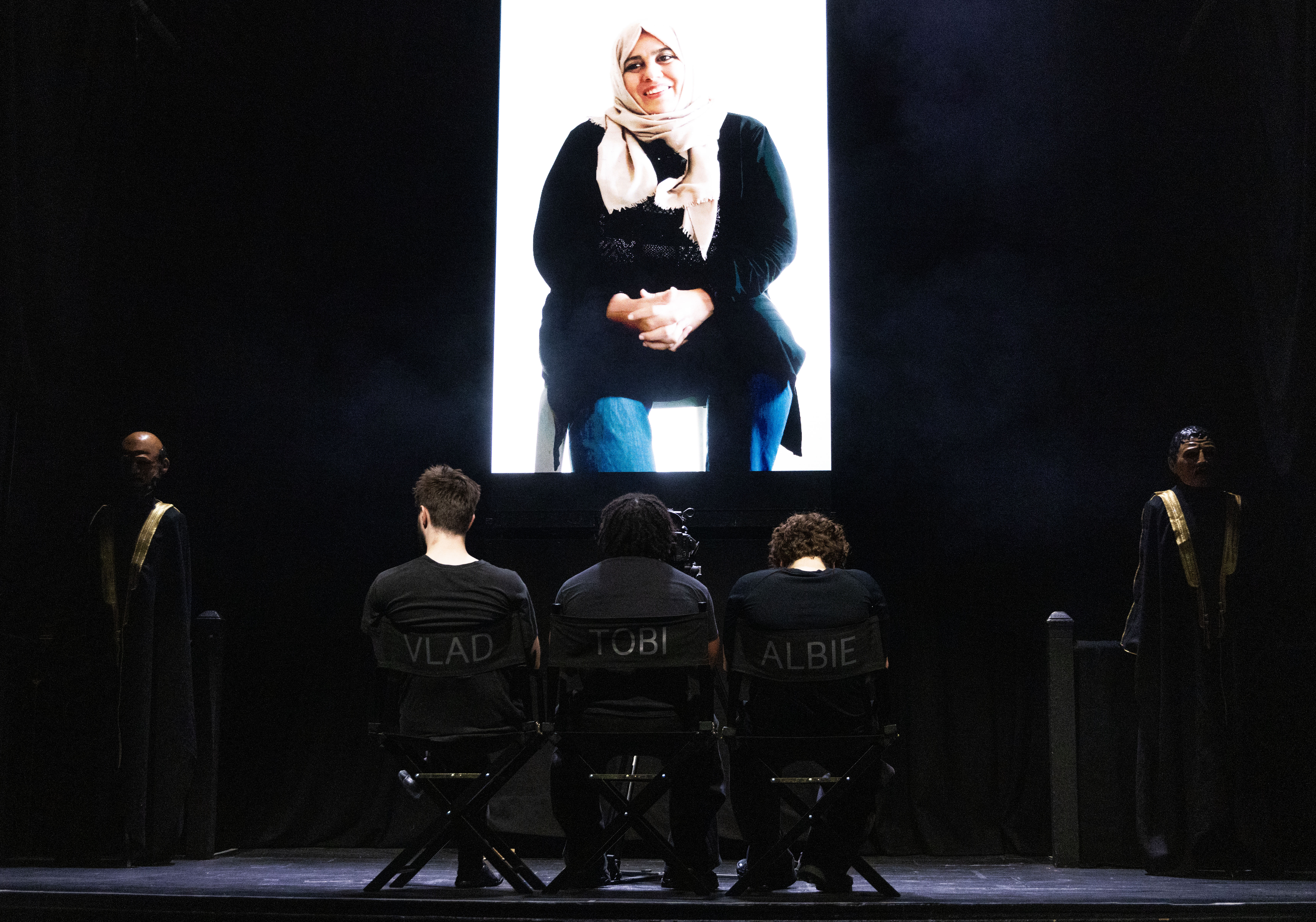 Syrian woman on a screen, with three young actors facing her